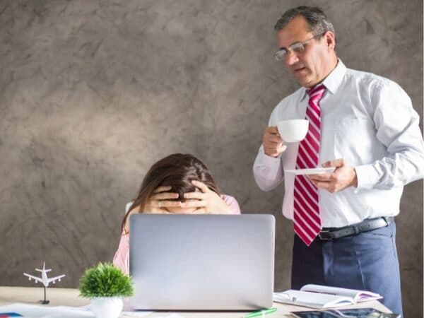 esempio di mobbing con un manager che guarda un dipendente con la testa tra le mani di fronte al computer