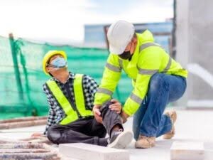 Operaio con gamba dolorante assistito da un collega dopo un infortunio sul lavoro